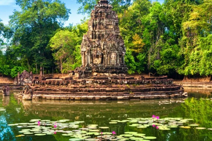 Neak Pean temple surrounded by a pool filled with blooming pink lotus flowers.