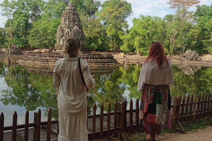 Twee toeristen kijken over een vijver naar de tempel Neak Pean.